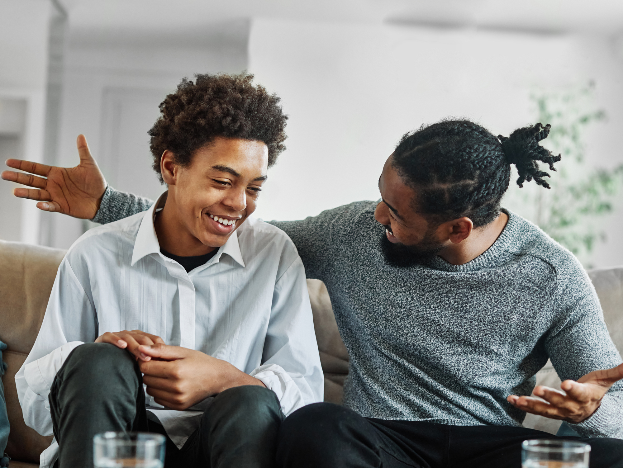 AdobeStock_593886551 Father and son talking on the couch with happy smiles